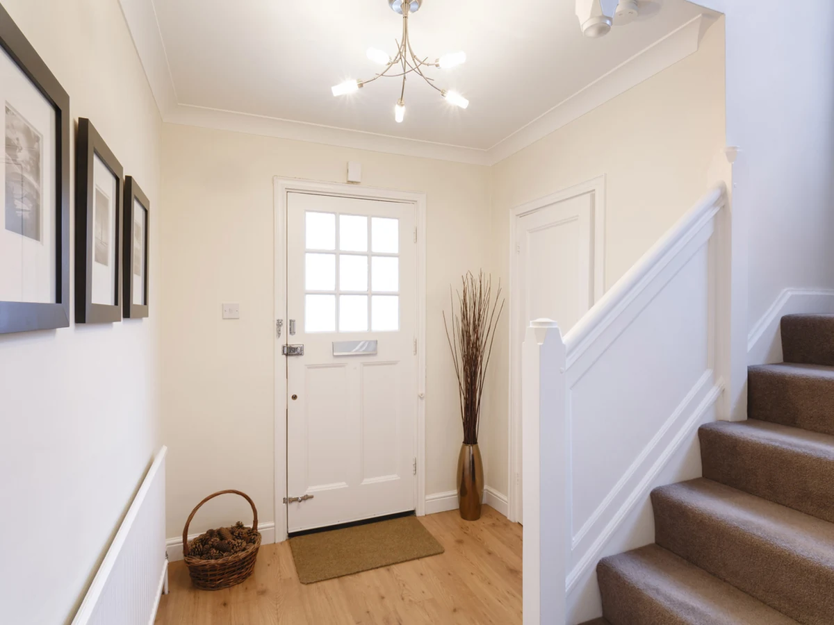 White hallway with a front door, framed pictures and a stair banister